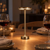 Gold cordless lamp on an oak dinner table with wine